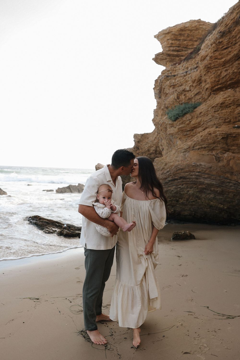 A romantic moment between a couple beneath a rocky coastal cave as ocean waves crash nearby.
