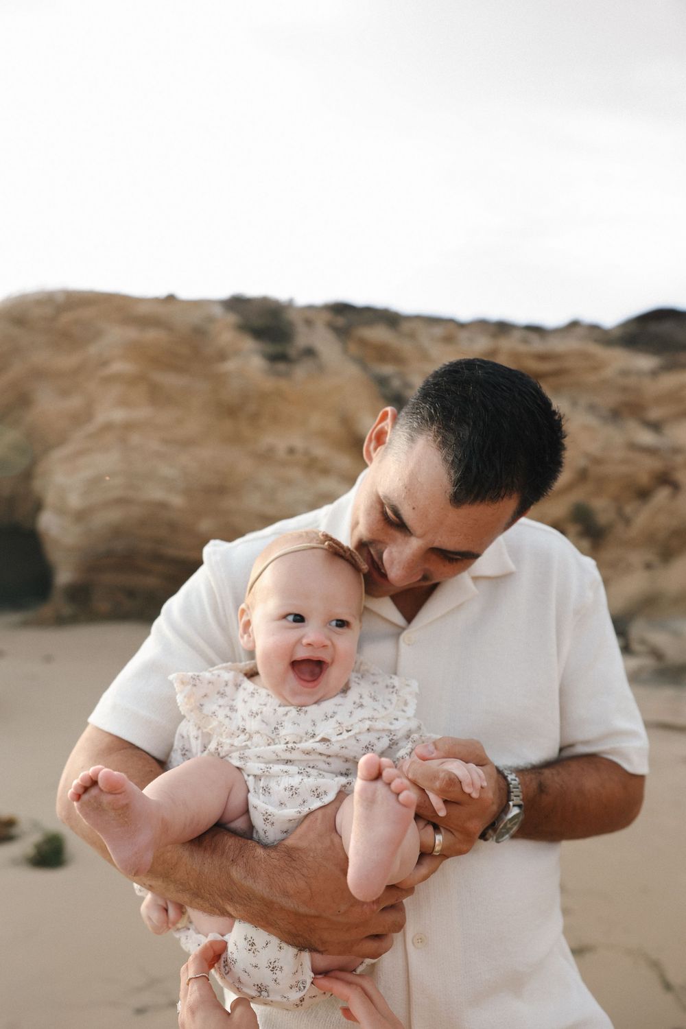 A parent and baby share joyful moments together while playing on a sandy beach at sunset.