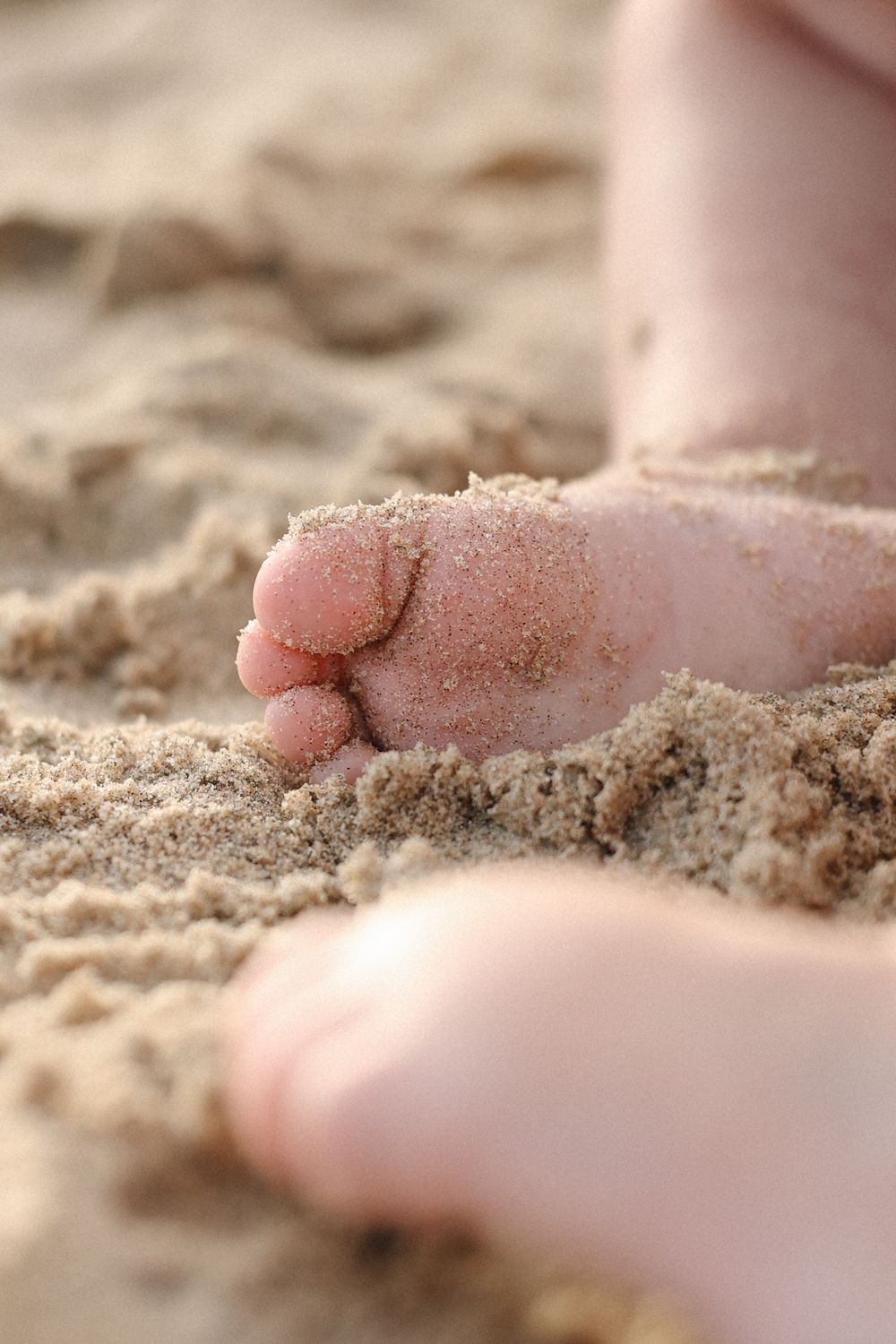 Close-up view of small sandy toes on a beach with fine grains of sand scattered across pink skin.