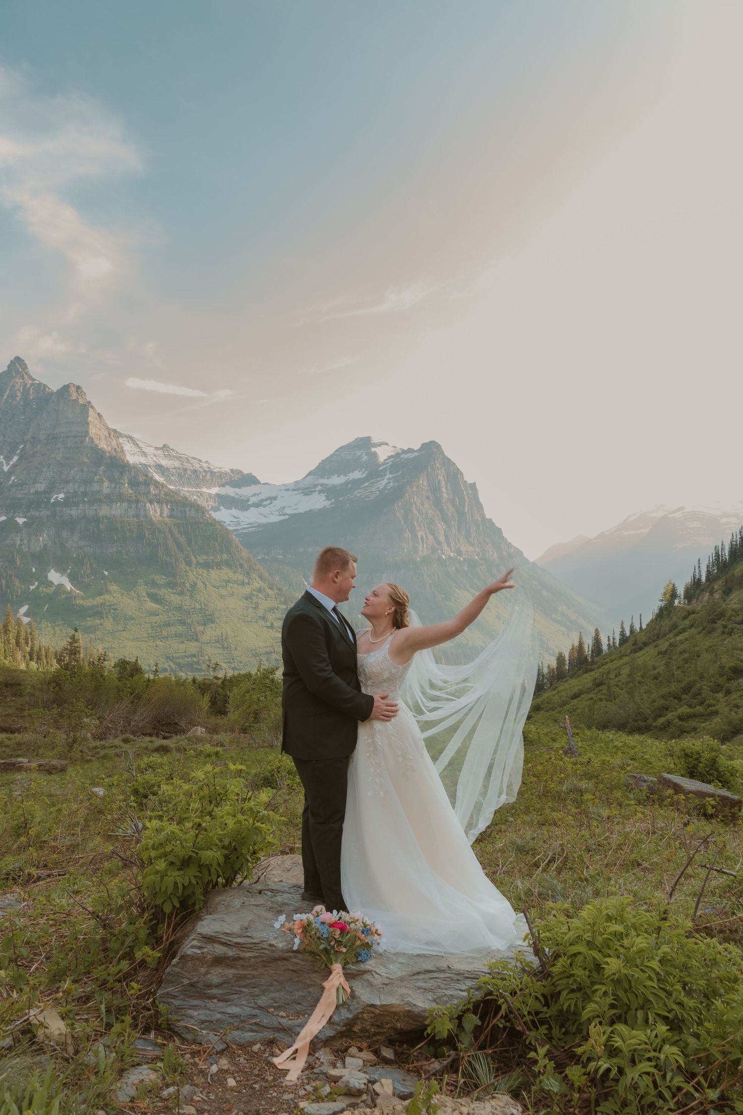 Dancing couple in wedding attire pose against dramatic mountain backdrop during sunset in the Canadian Rockies.