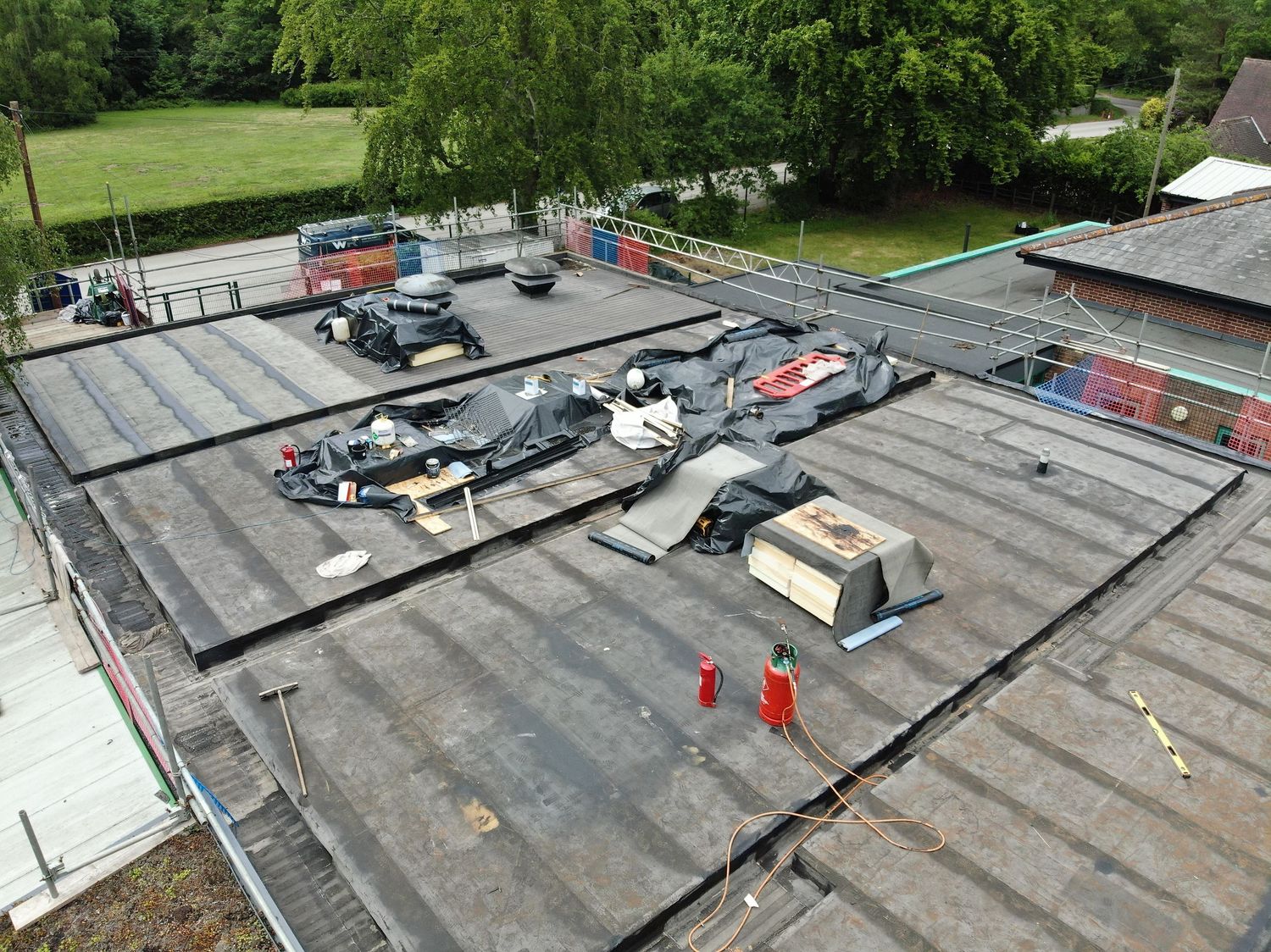 Aerial view of construction workers on a flat commercial roof with equipment and materials during renovation project.