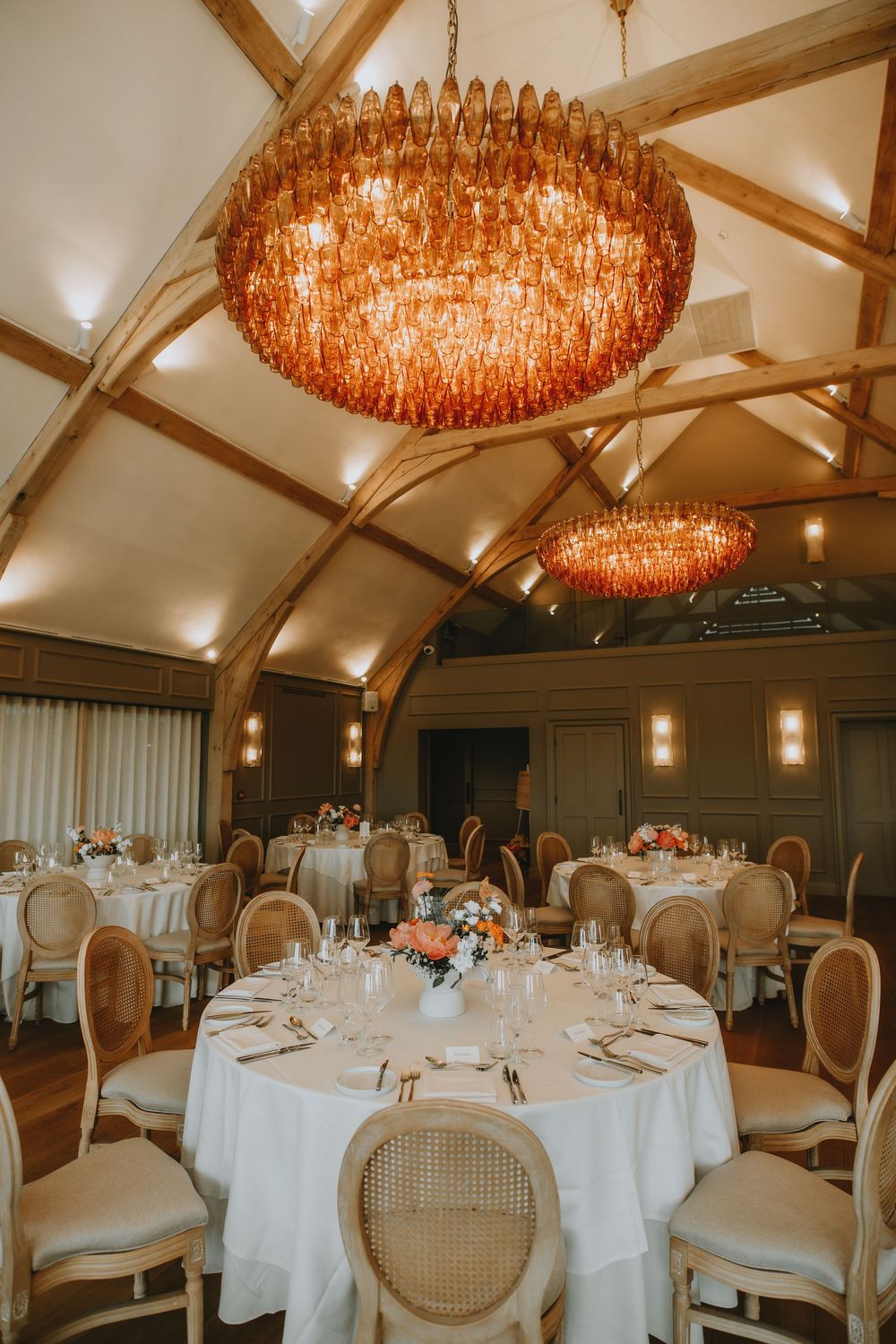 Elegant wedding reception room with amber crystal chandeliers, arched ceiling beams, and round tables with white linens.