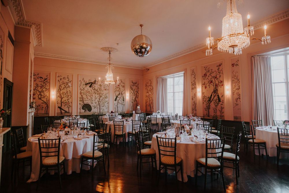 Elegant ballroom dining room with pink walls, crystal chandeliers, and round tables set for a formal dinner service.