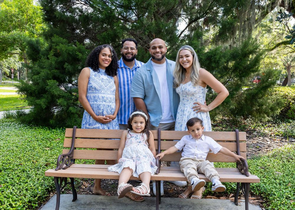 A family sitting on a wooden bench in a garden setting wearing coordinated light blue and floral outfits.