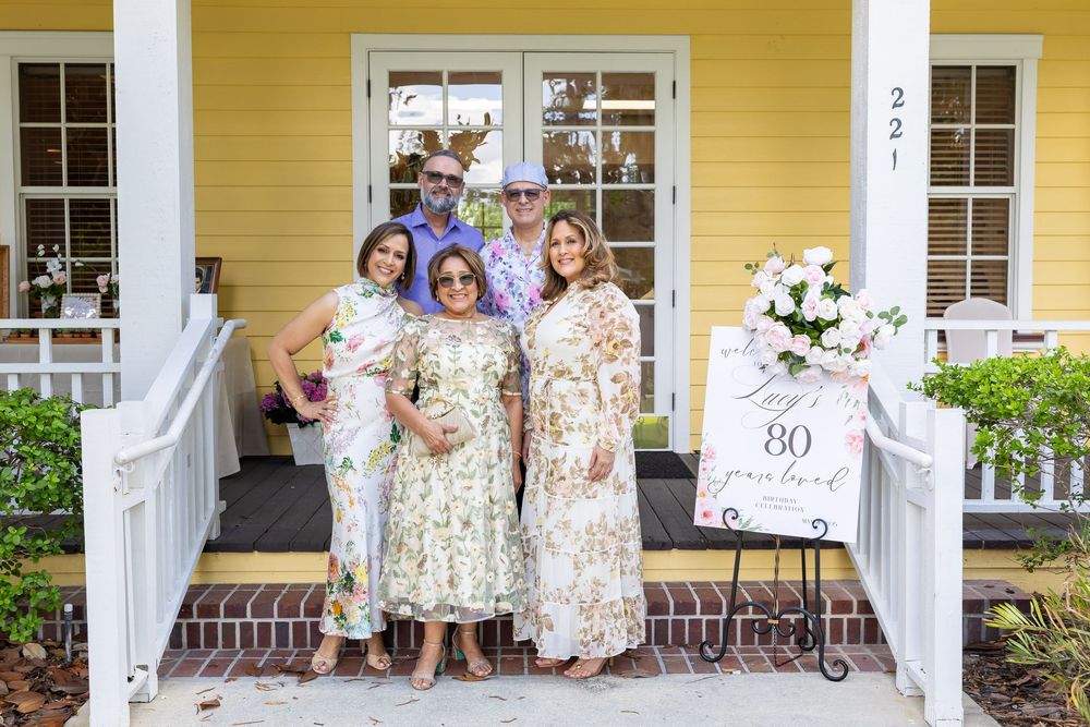 Family celebration photos in front of a charming yellow house with white trim.