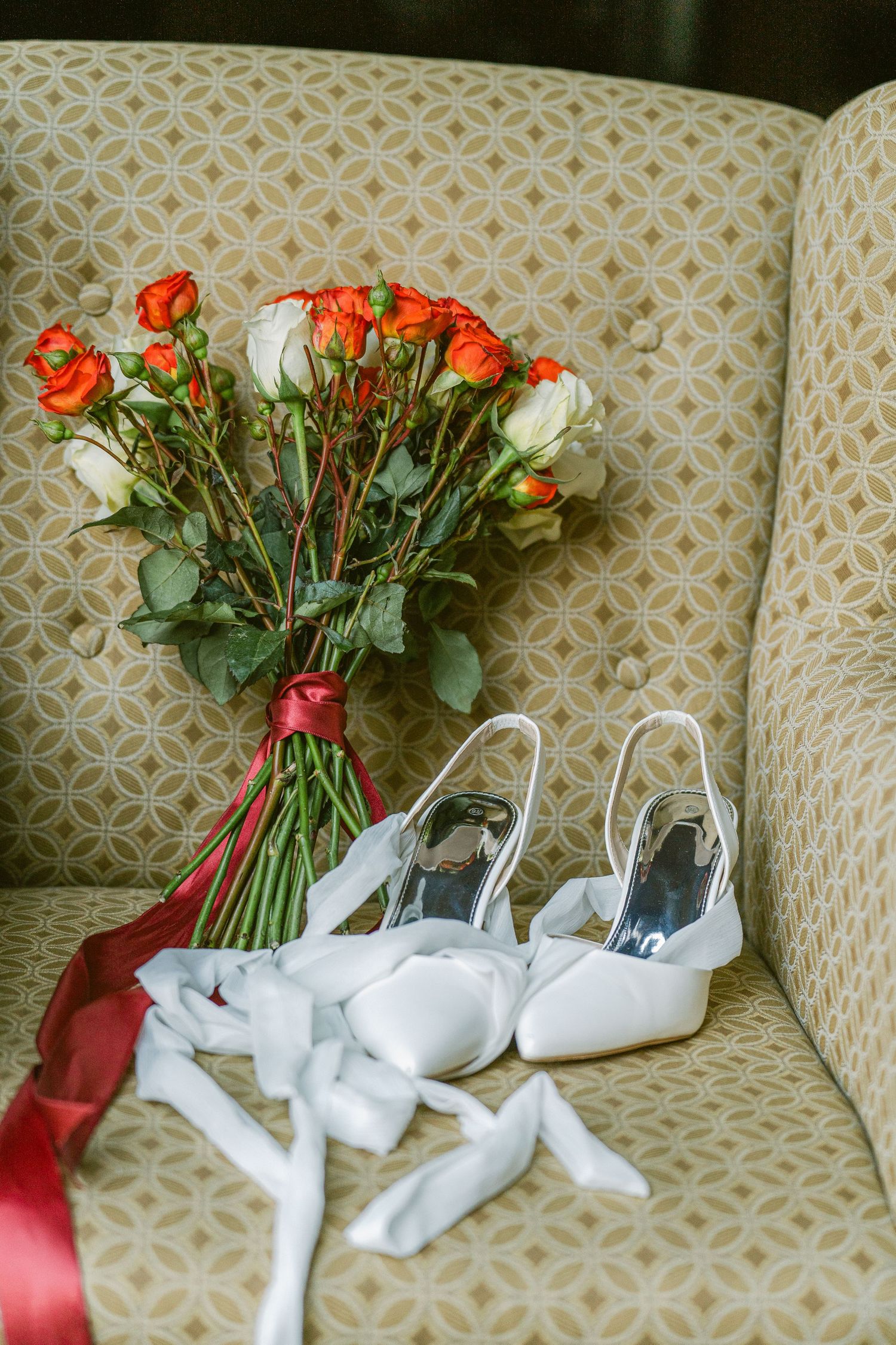Close-up of a red and cream garden-style bridal bouquet paired with white ribbon wedding shoes, styled on a vintage chair in St. Paul, MN