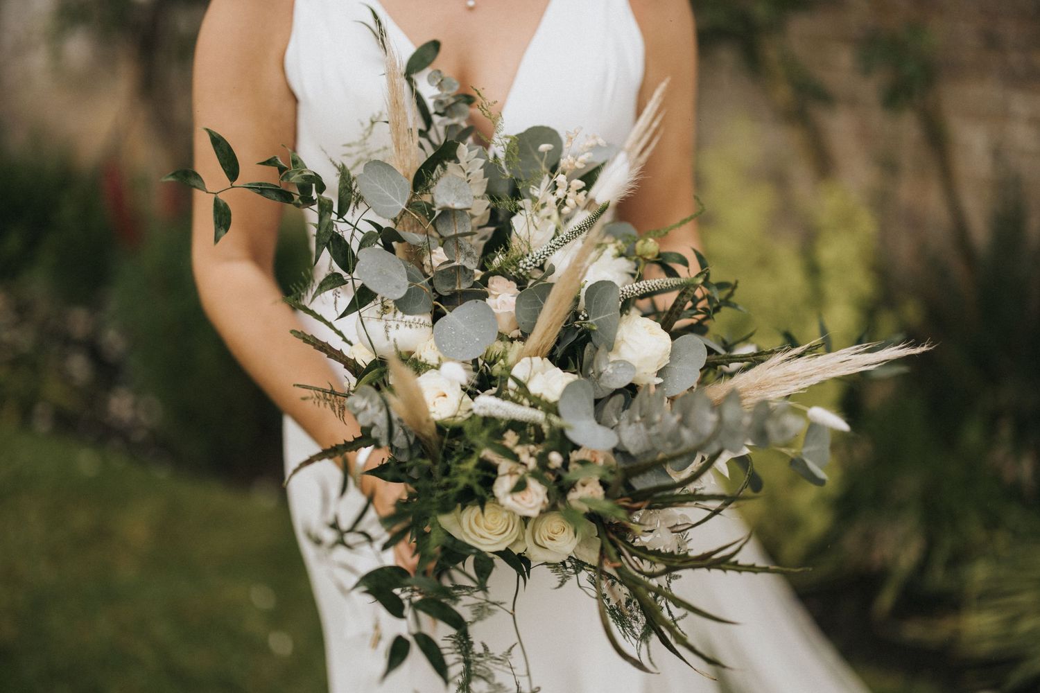 A close-up of an elegant white and green wedding bouquet with eucalyptus leaves and delicate flowers.