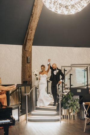 Couple celebrates joyfully while descending elegant stairs under spherical light fixture at Grand Lodge Oaklands - by Grimsby photographer.