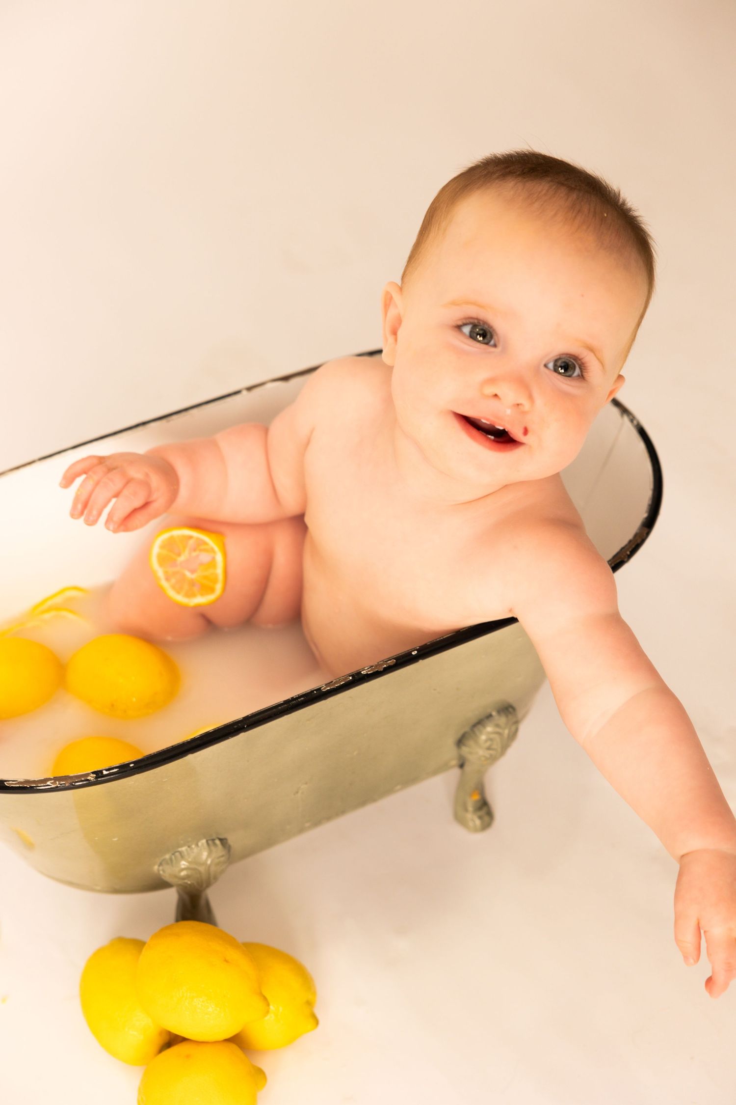 Smiling baby in vintage-style bathtub with fresh yellow lemons scattered around.