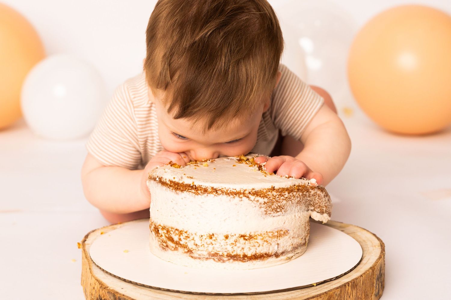 A toddler eating a thin flatbread with visible bite marks on a white plate against a peach-colored background.
