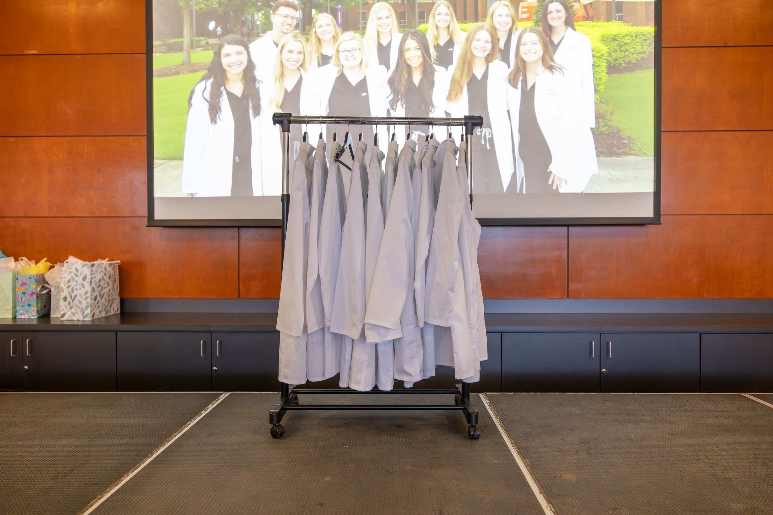 A group wearing white choir robes stands together in a lobby area with orange walls.