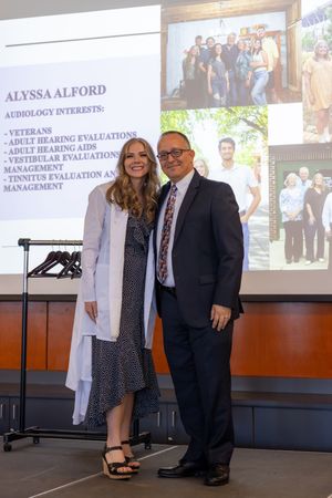 Professional presentation slide showing audiology interests and specialties with two people standing together at a podium.