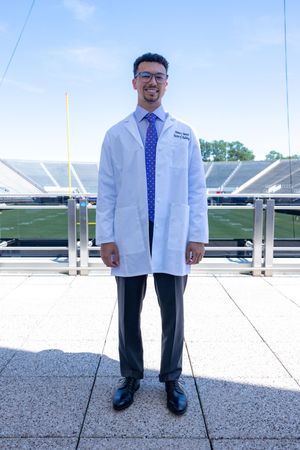 Medical professional in white coat and polka dot tie standing on stadium balcony overlook.