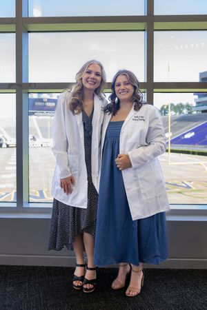 Two medical professionals in white coats pose together near stadium windows.