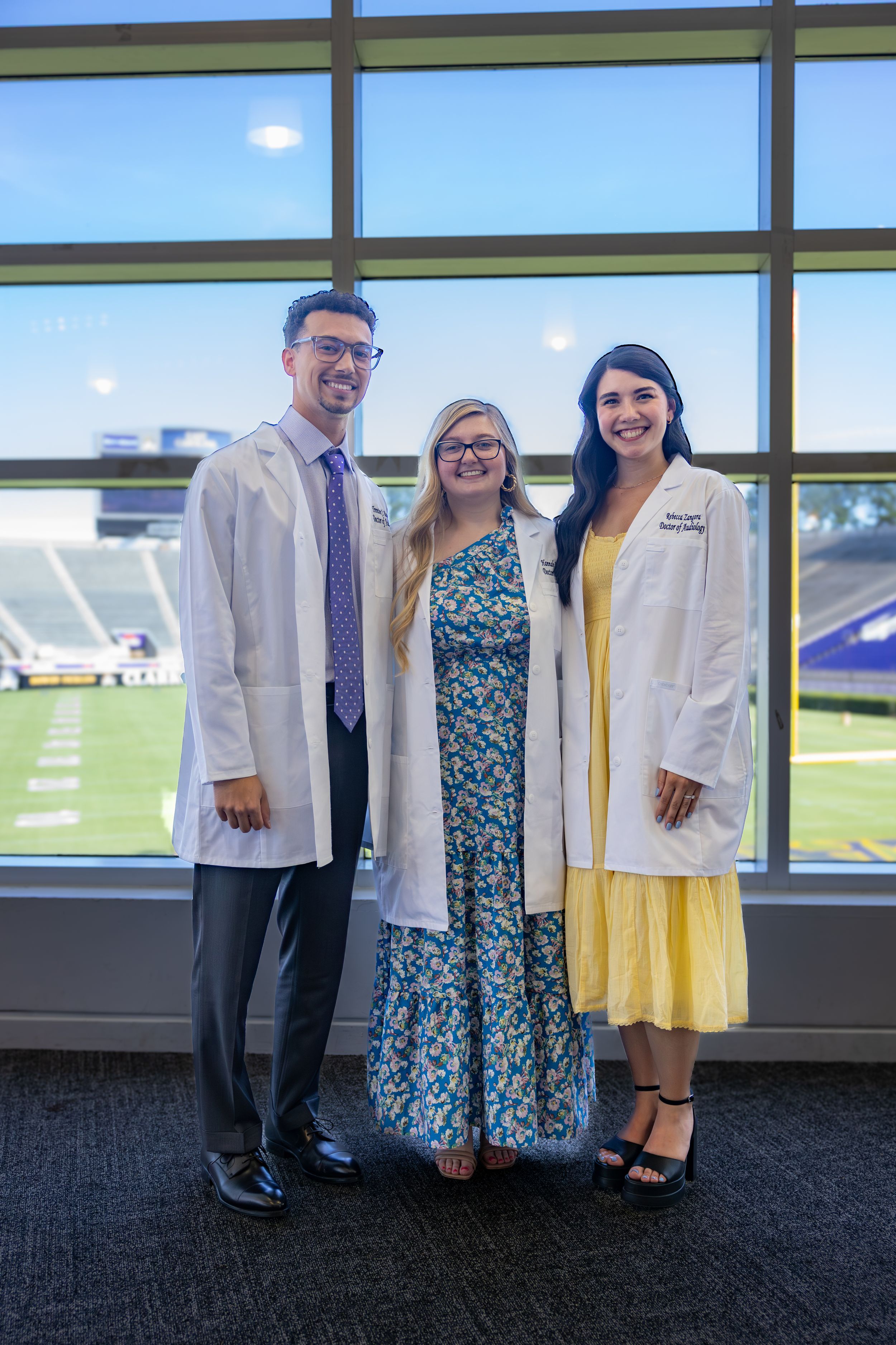Medical school graduates in white coats celebrate with family members during commencement ceremony.