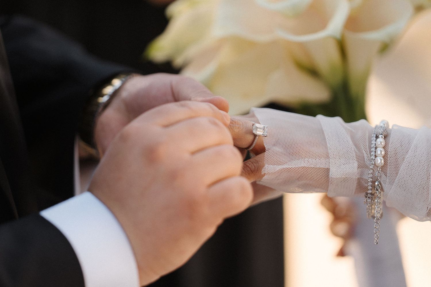 Two pairs of hands exchange a wedding ring in a close-up shot during a marriage ceremony.