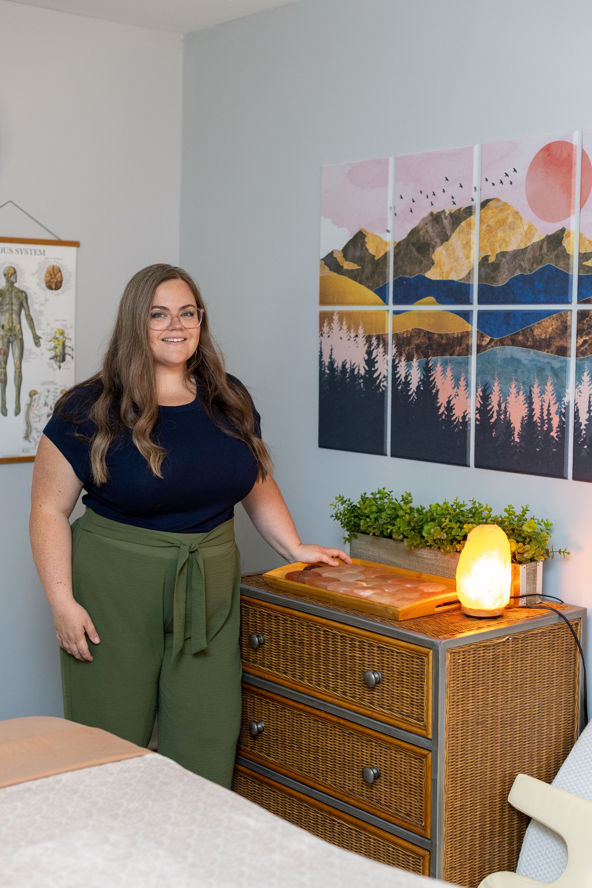A room decorated with mountain art prints features rattan furniture, a table lamp, and green accent pieces.