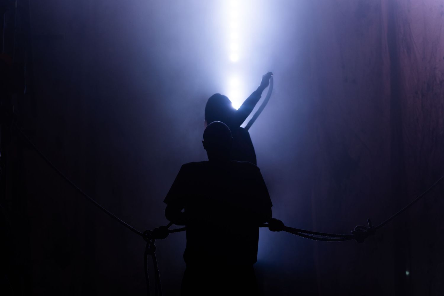 Dramatic silhouette of performers on a dimly lit stage with atmospheric lighting effects.