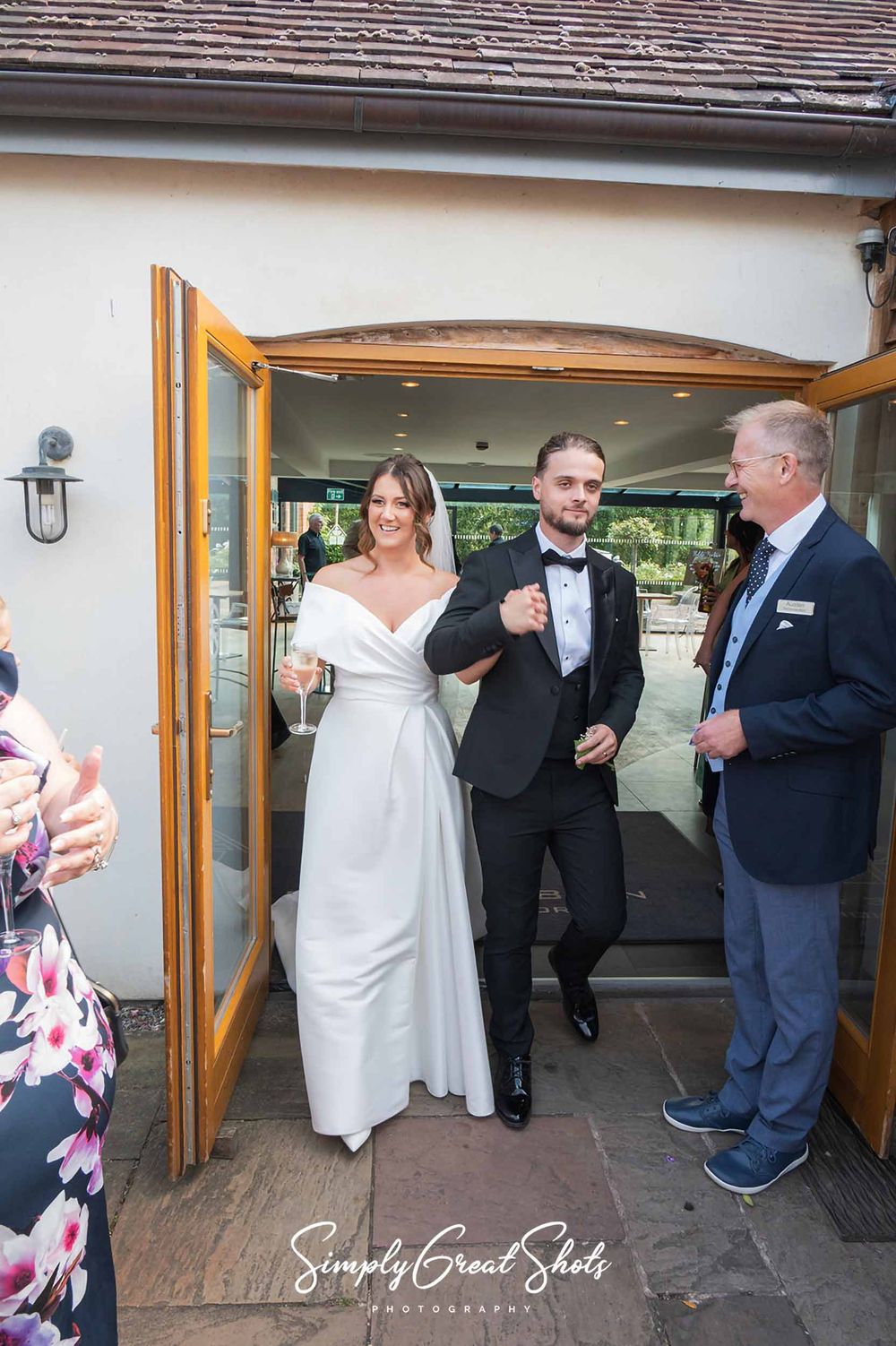 A bride in a white gown and groom in a black tuxedo exit through wooden doors at the back of Redhouse Barn wedding venue.
