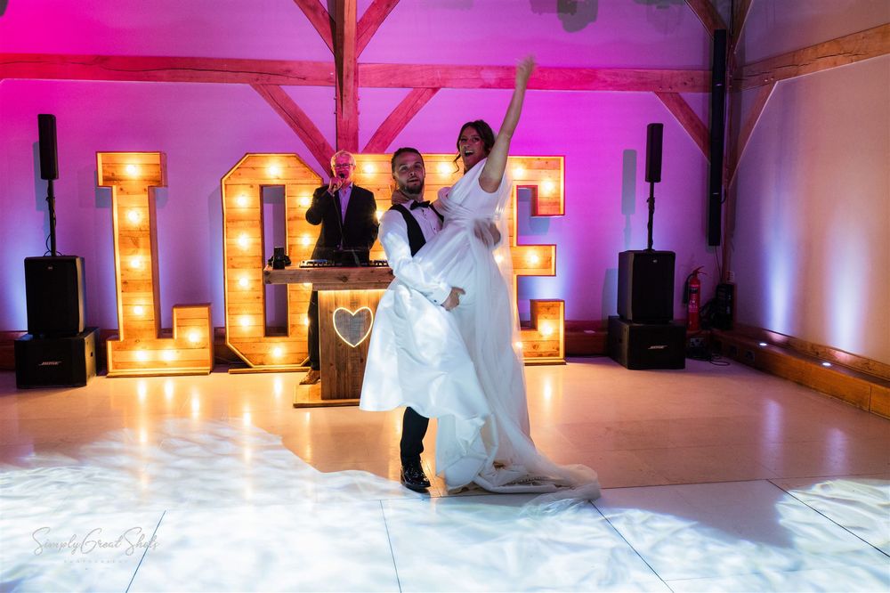 A couple on their first dance at a wedding reception with illuminated LOVE letters glowing in the background, at Redhouse Barn wedding venue