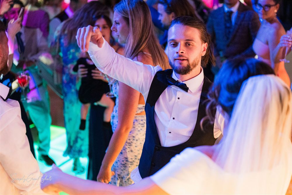 A groom and his guests dance and celebrate at a lively wedding reception with colourful mood lighting at Redhouse Barn wedding venue