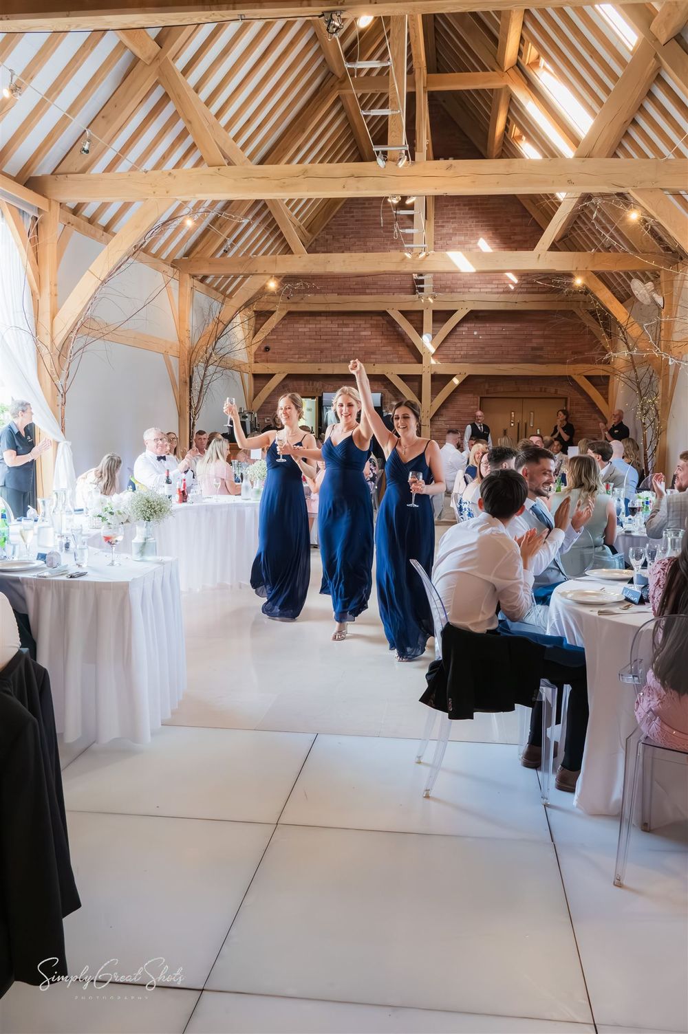 The bridesmaids and maid of honour enter into a rustic wooden barn venue decorated with elegant white linens and blue accents.
