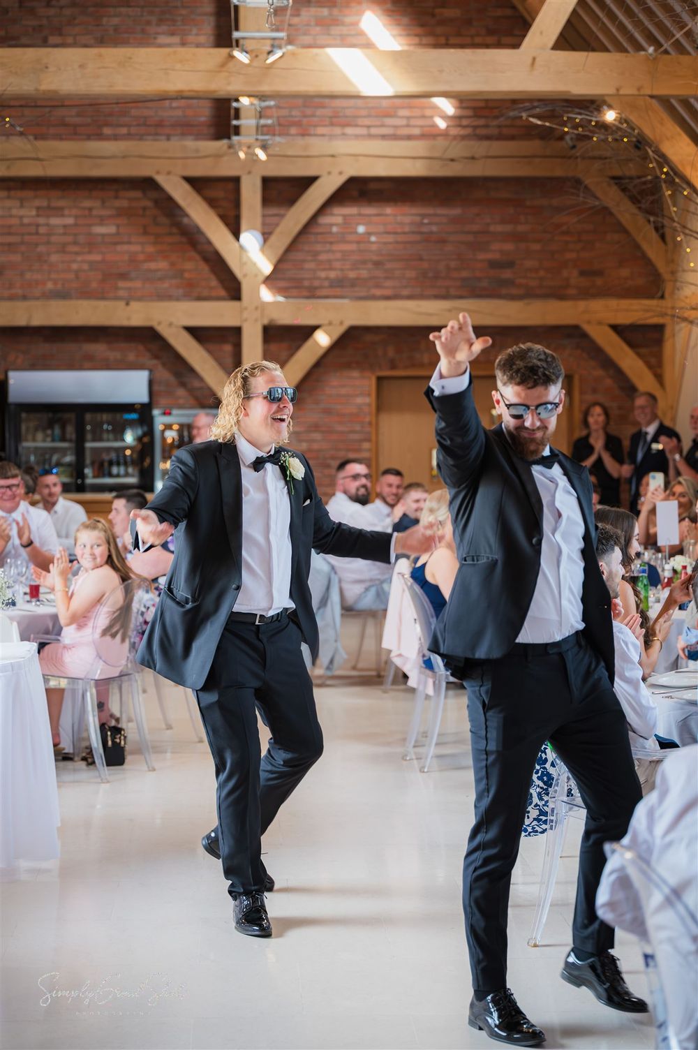 The two best men in tuxedos enthusiastically dancing at a wedding reception in Redhouse Barn. A rustic barn venue with exposed beams.