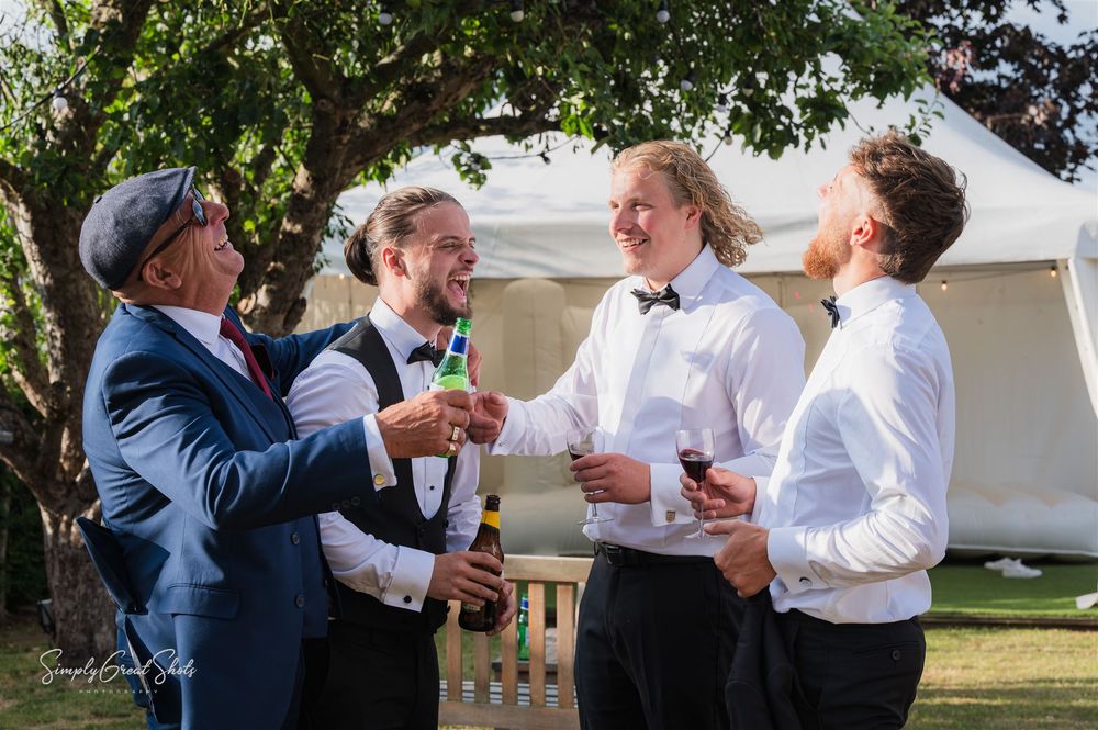 Redhouse Barn Wedding Venue Groomsmen in formal attire sharing drinks & laughs outdoors at a wedding reception SimplyGreatShots Photography.
