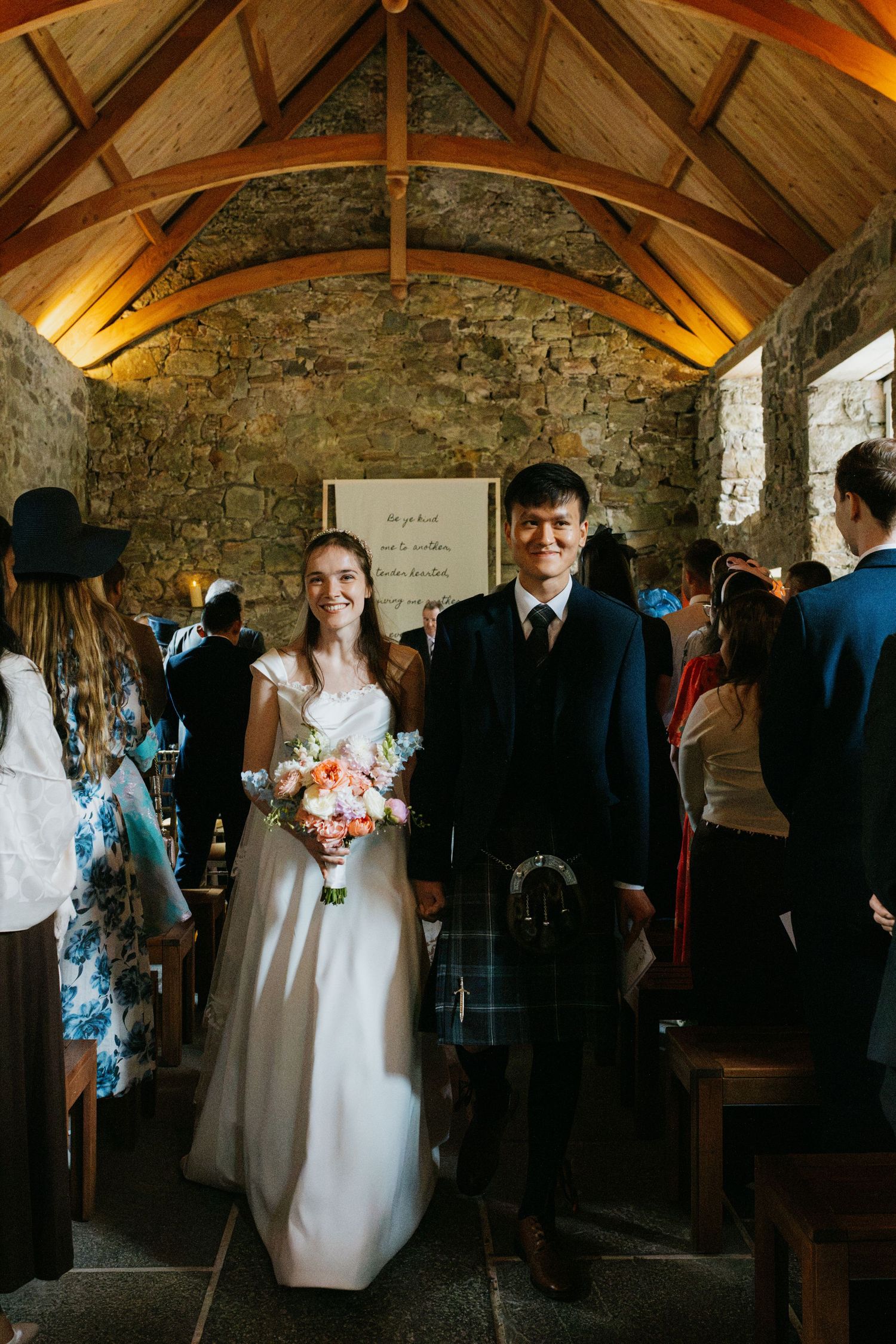 Historic stone mansion with guests gathered on the sprawling lawn under blue skies.