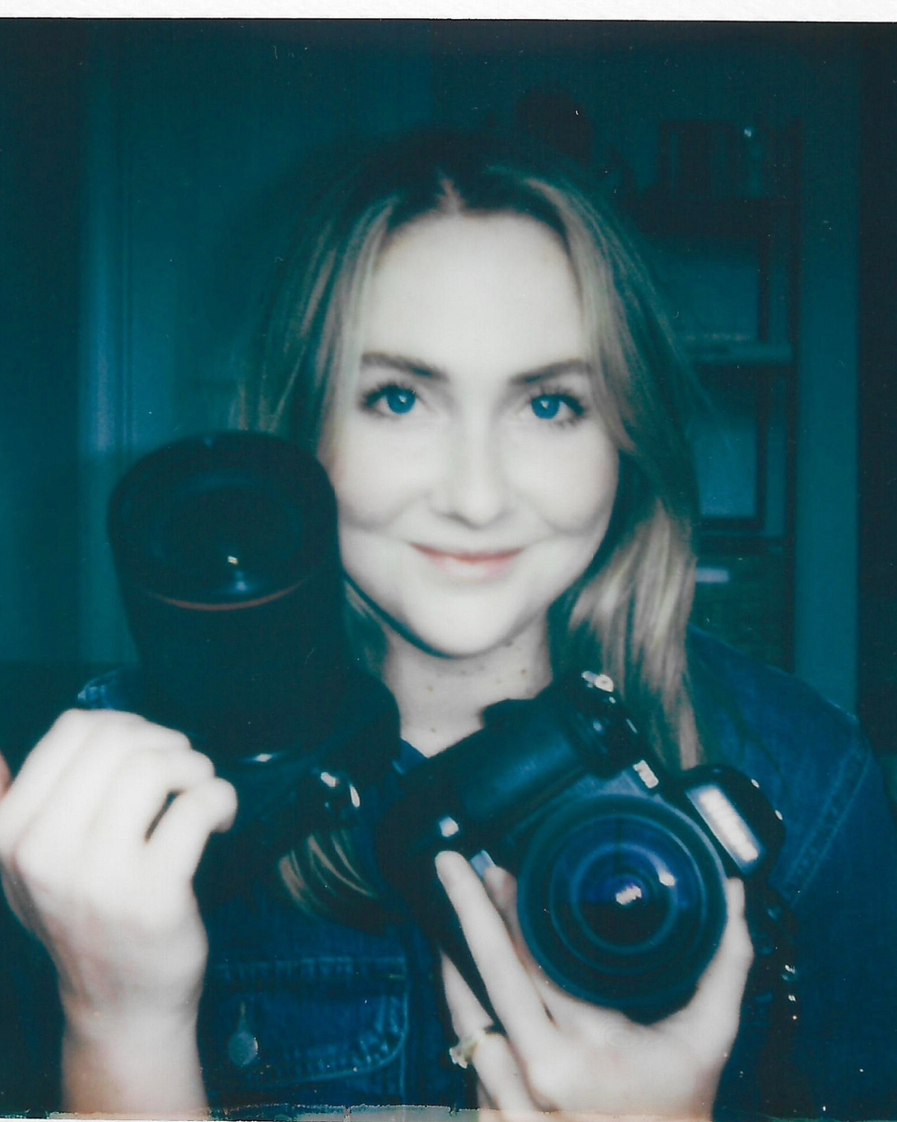 A person showing off photography equipment including a professional camera and lens against a dark teal background.