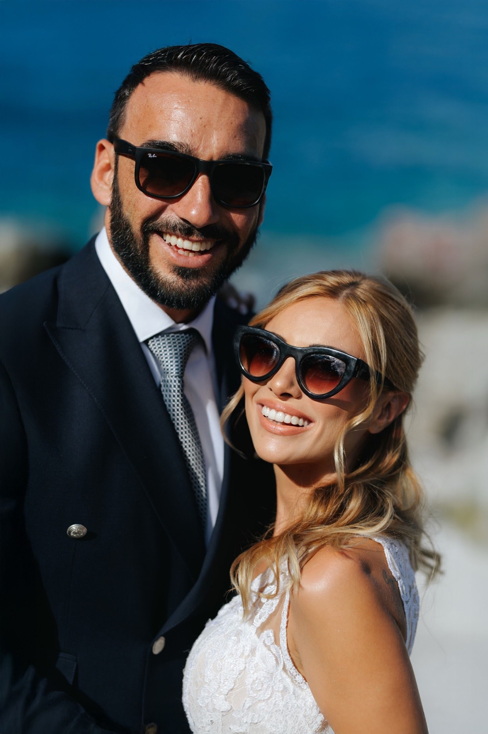 Happy couple enjoying a sunny beach wedding day with the bride in white and groom in dark suit and sunglasses.