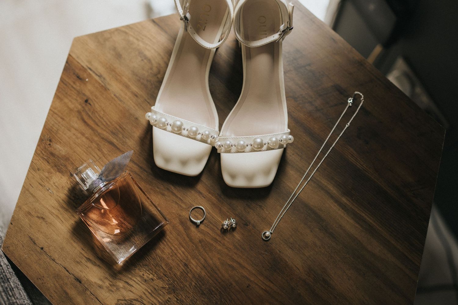 Wedding accessories including sparkly silver flats, lace veil, invitation and wedding ring displayed on wooden surface.