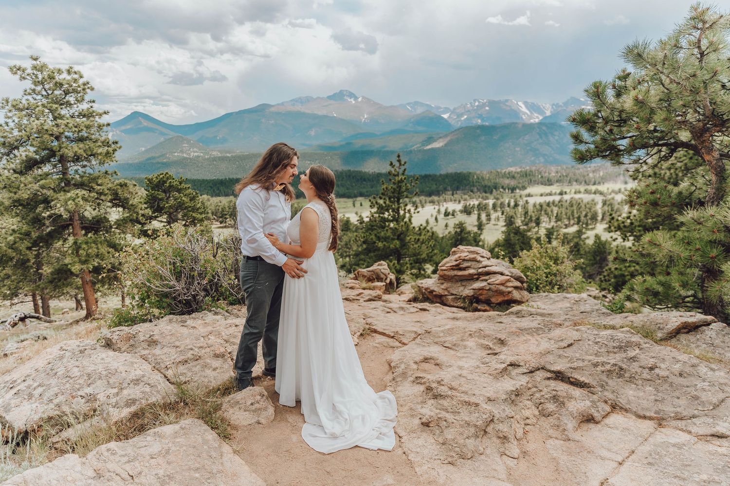 couple standing on rocky ledge at 3M Curve, sweeping mountain views in RMNP, dramatic Colorado elopement backdrop