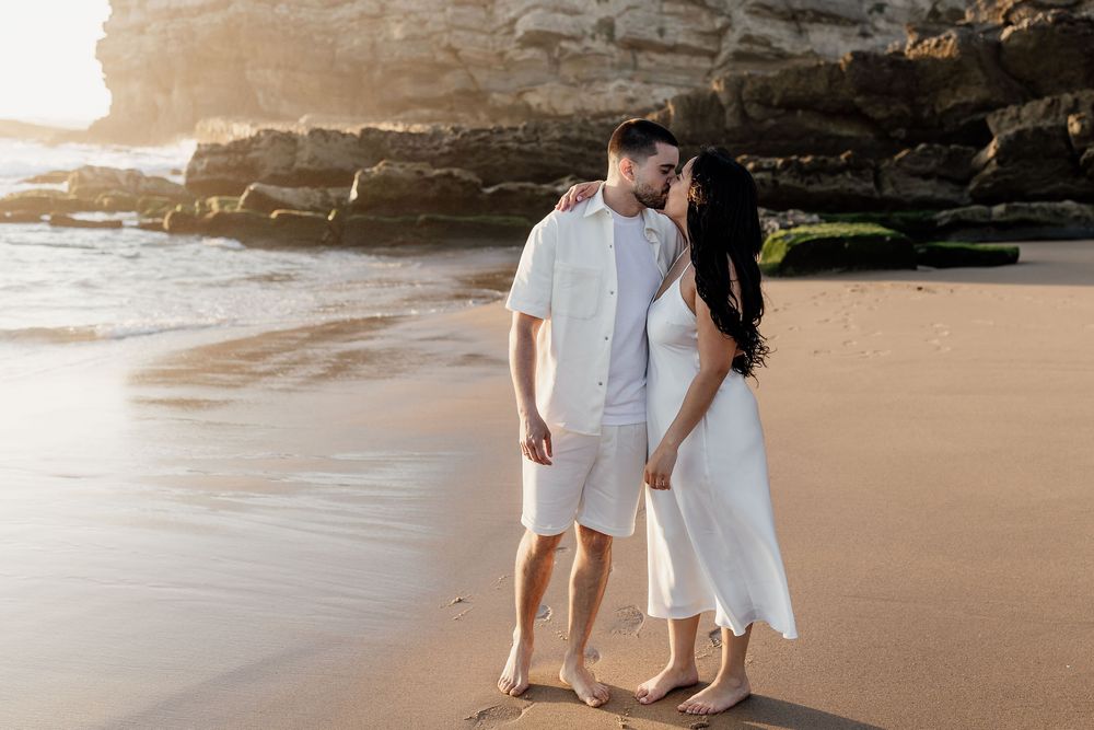 A romantic couple shares tender moments on a sandy beach during sunset while walking along the shoreline.