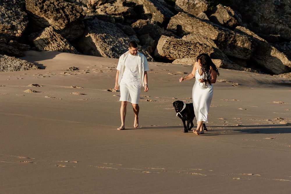 People standing on a beach near rocky outcrops during sunset in warm lighting.