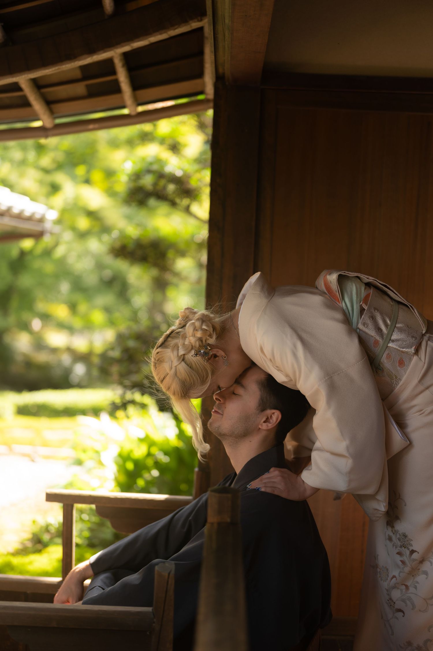 Couple in traditional Japanese wedding attire sharing a tender kiss in a garden setting.