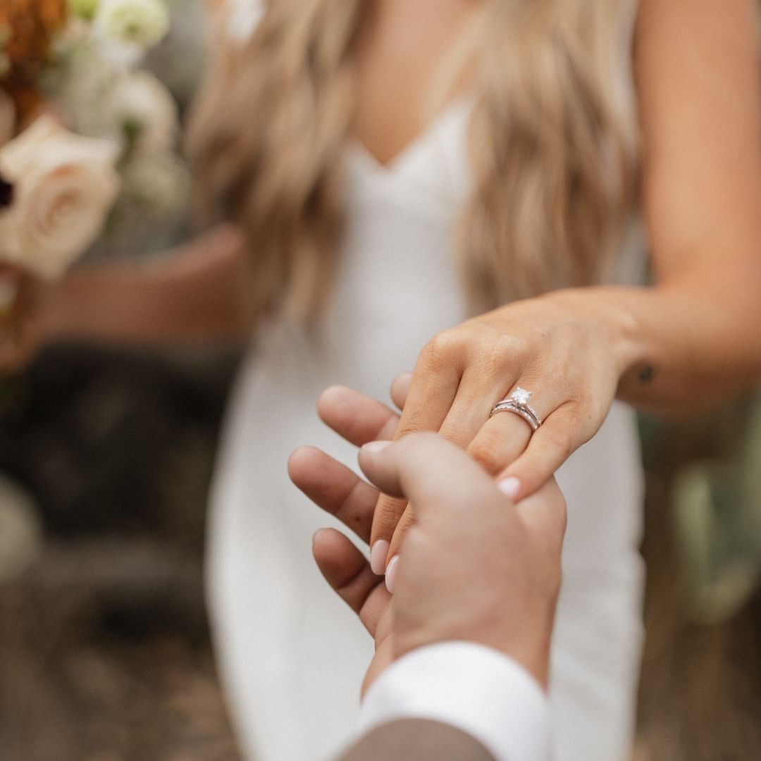 Close up of hands showing wedding rings with white wedding dress and floral bouquet in soft focus background.
San Diego wedding photographer