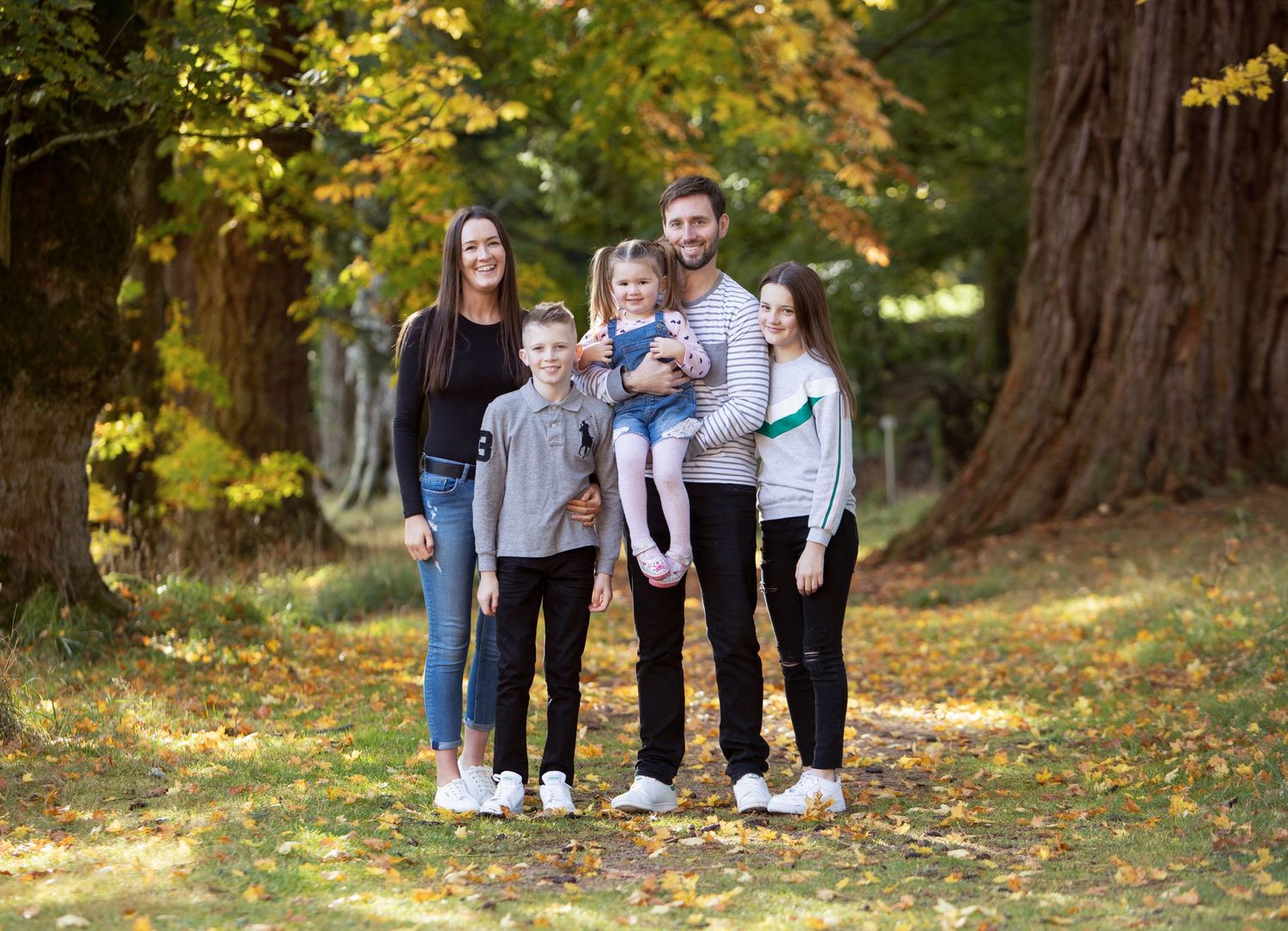 Happy family of five posing together in a scenic autumn woodland setting.
