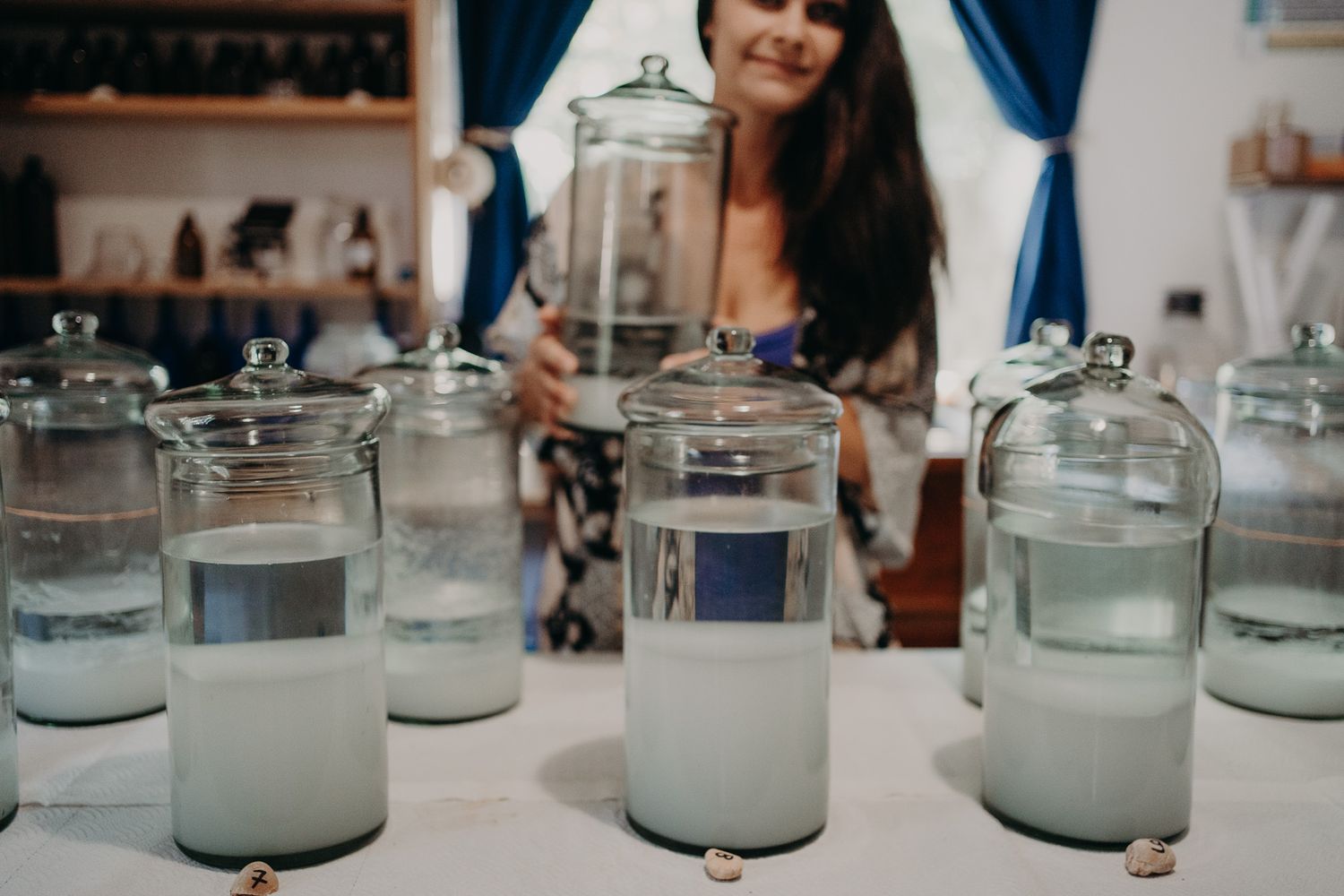 Line of glass candle jars arranged on white surface with blue curtain accent.