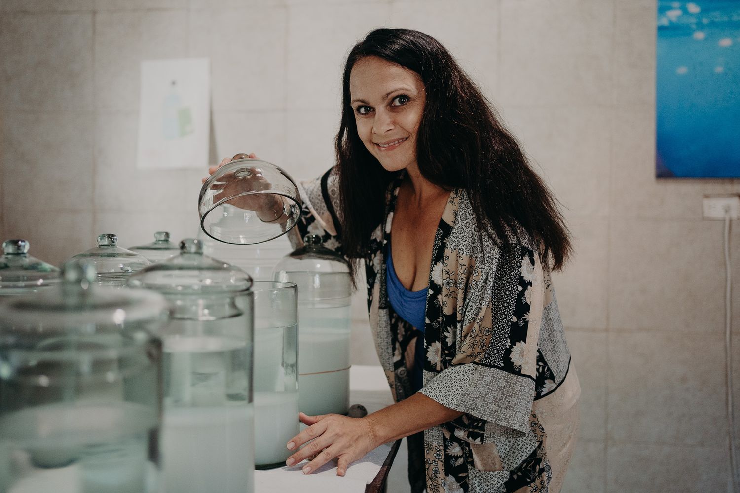 Woman smiling while handling glass containers in a bright kitchen workspace.