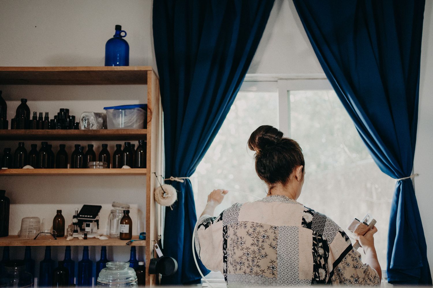 View from behind of someone working at a counter with blue curtains and shelving visible.