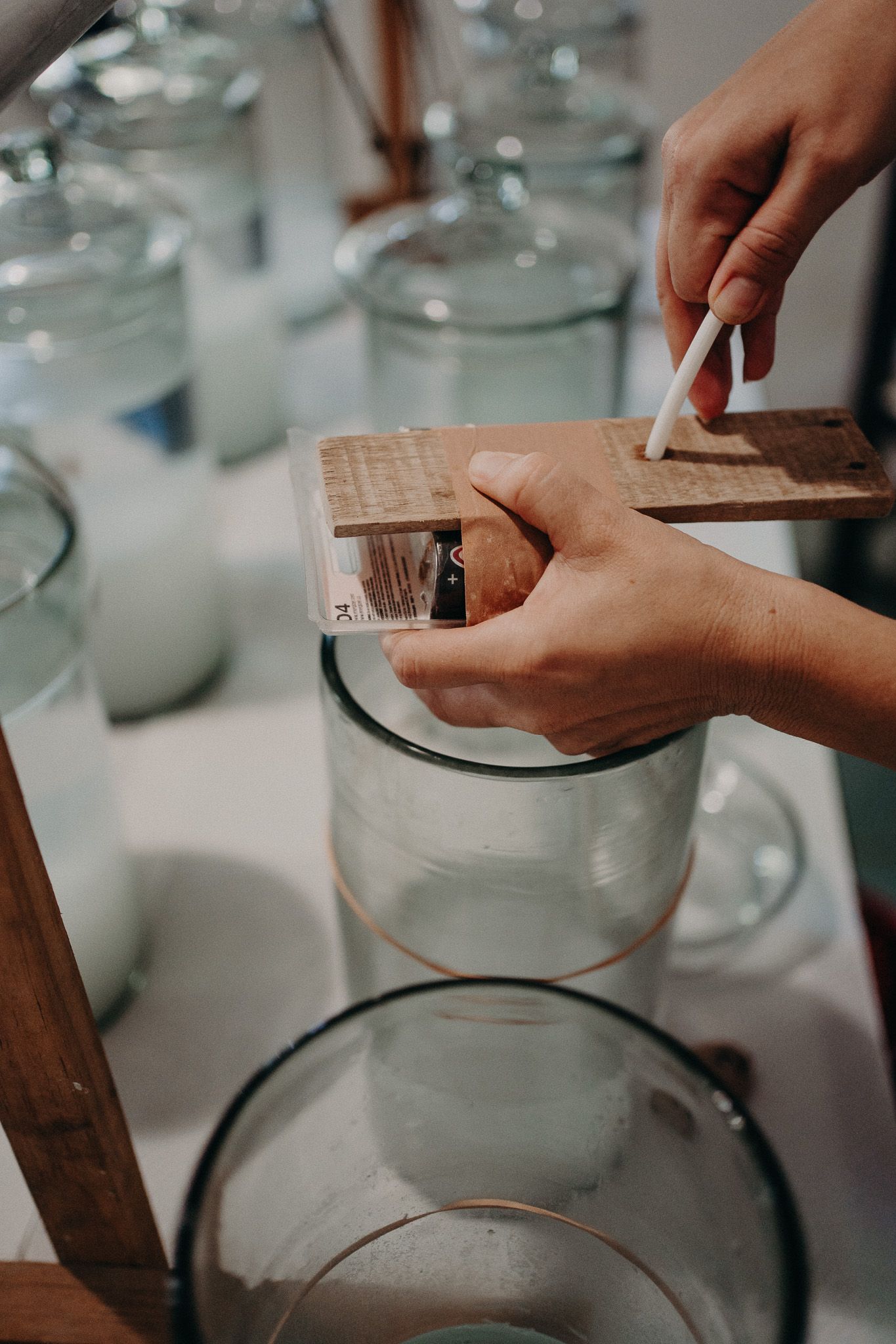 Hands measuring ingredients with wooden tools over glass containers on white counter.