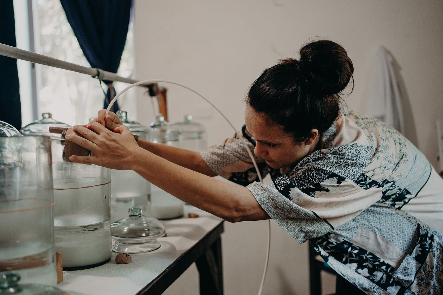 Person in patterned dress carefully working with laboratory-style glass containers.