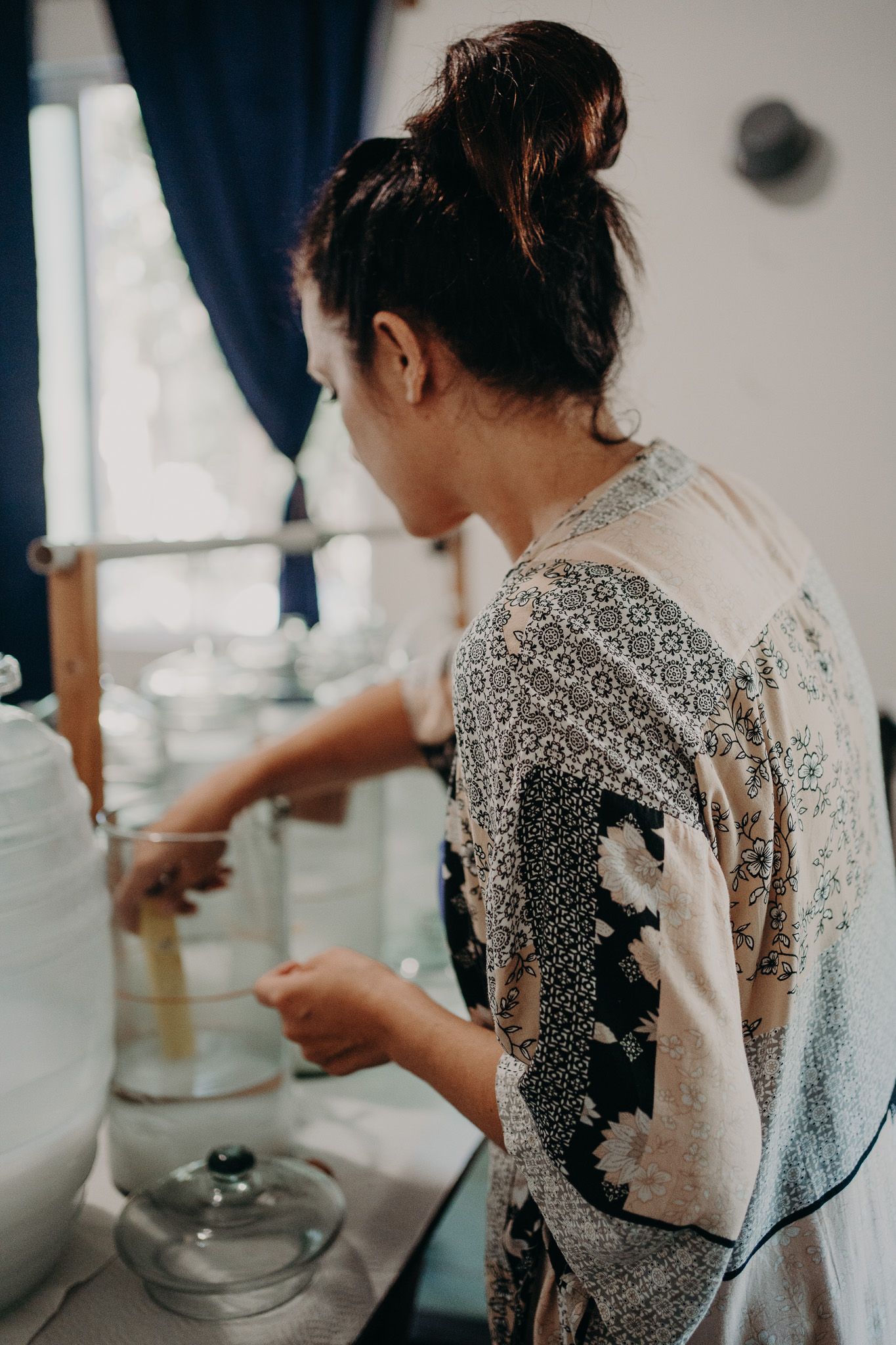 Someone wearing a patterned kimono-style garment working with glass containers in a kitchen setting.