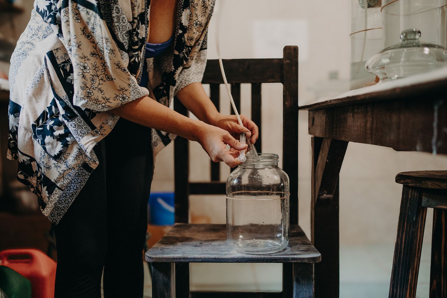 Hands working with glass containers on a dark wooden chair in an indoor setting.