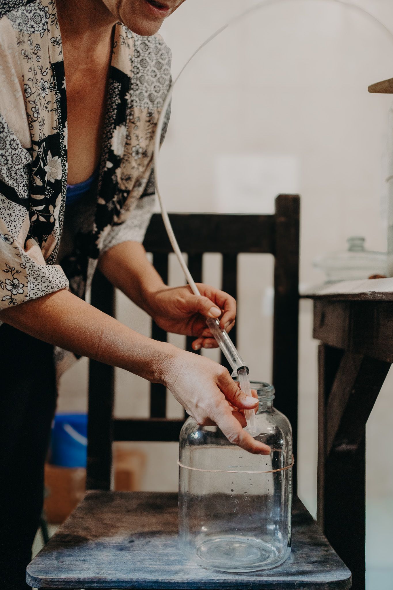 Close-up of hands pouring liquid into a clear glass container on a wooden surface.