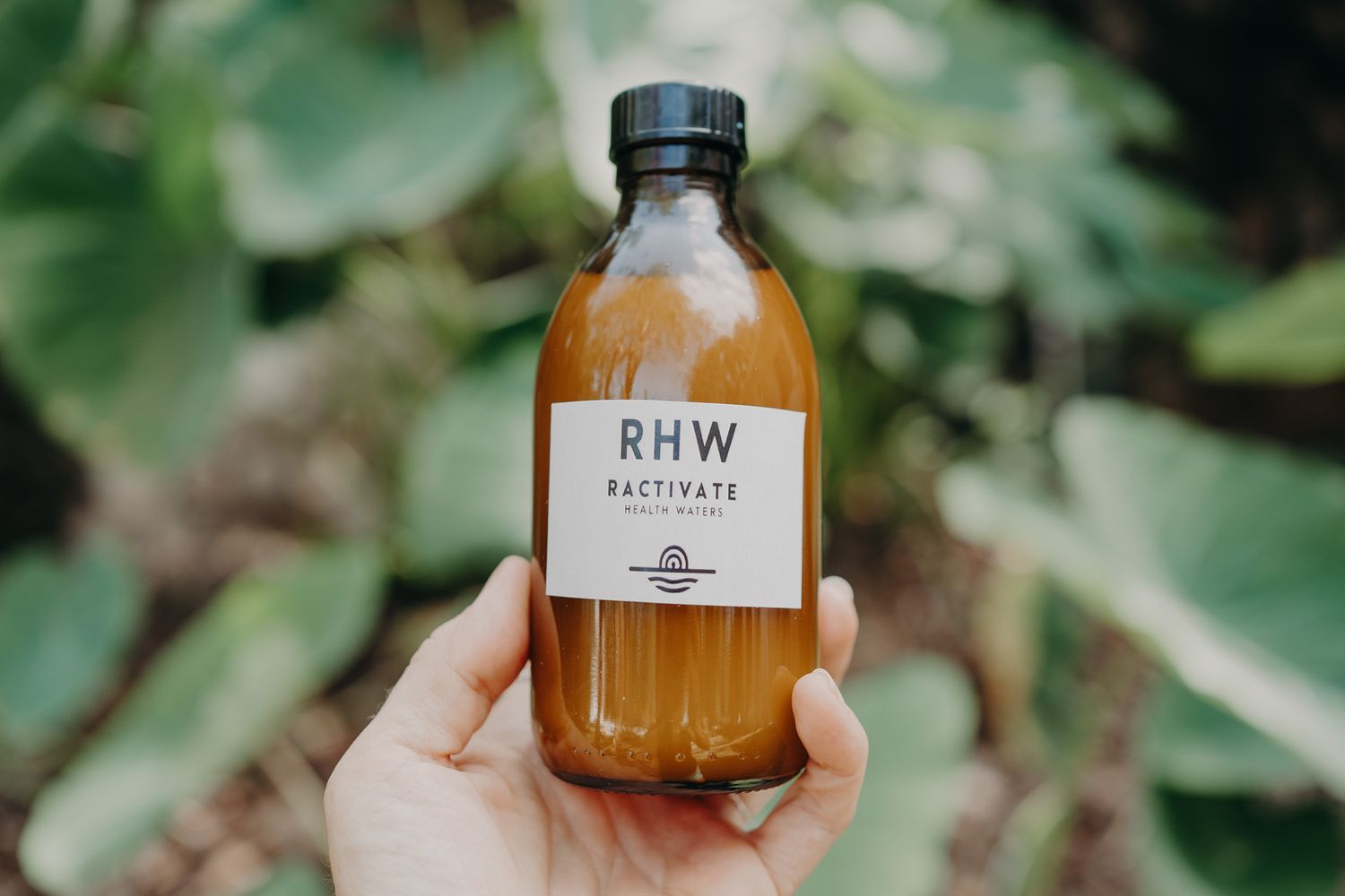 Brown glass bottle labeled RHW held up against green foliage background.