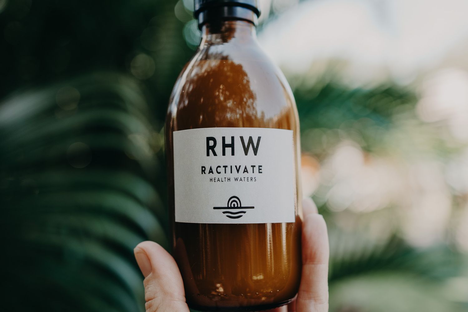 Close-up of RHW branded brown glass bottle held against blurred green background.