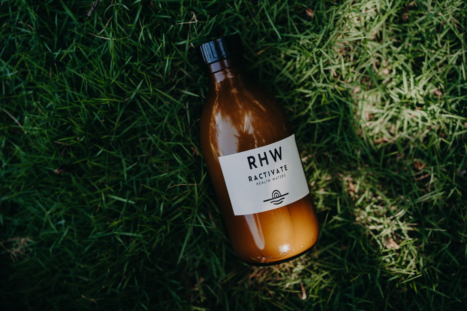 Brown glass bottle labeled RHW lying on green grass in sunlight.