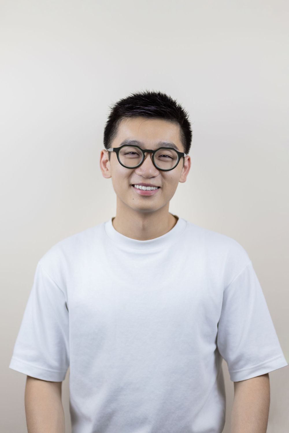 Casual portrait of young man in white t-shirt and glasses against neutral background.